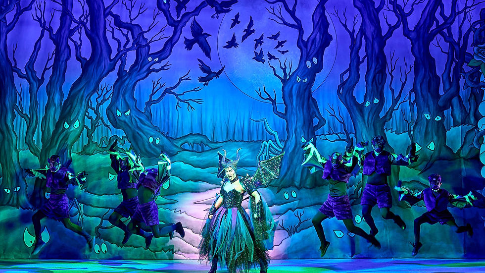 A performer in a horned costume dances with masked dancers in a mystical forest stage, featuring purple lighting and eerie trees with eyes.