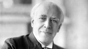 Konstantin Stanislavski: An elderly man in a suit smiling subtly in a black-and-white photo. Soft focus background, conveying a calm, reflective mood.