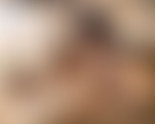 Woman writing in a book at a wooden table, surrounded by stacked books. Sunlight streams through a window, creating a warm, focused mood.