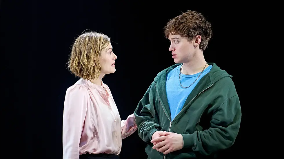 A woman in a pink blouse and a man in a green hoodie converse intensely against a black background, conveying a serious mood.