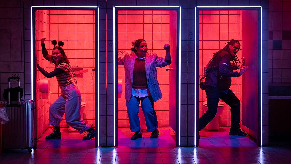 Three women pose in glowing pink bathroom stalls, fists raised, with luggage at left; energetic, dramatic neon scene.