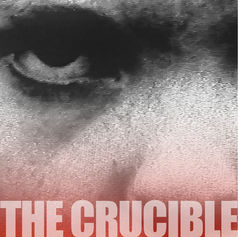 Close-up of an intense eye in grayscale with a red tint. The text "THE CRUCIBLE" is in bold white at the bottom, conveying a dramatic mood.