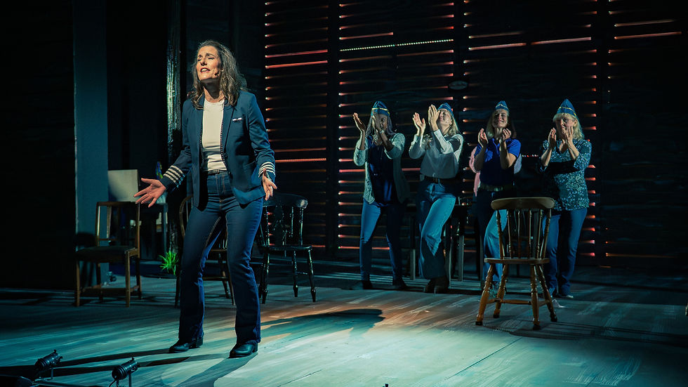 A woman in a pilot uniform performs passionately on stage, while four people clapping stand in the background. The lighting is dramatic.