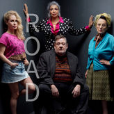Four people pose against a dark background. "ROAD" is vertically on the left. The mood is serious. Bright and patterned clothing. Road at the Royal Exchange Theatre, Manchester