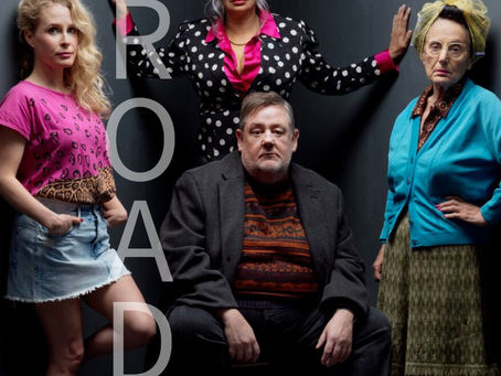 Four people pose against a dark background. "ROAD" is vertically on the left. The mood is serious. Bright and patterned clothing. Road at the Royal Exchange Theatre, Manchester
