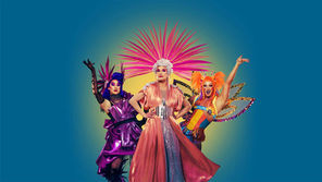 Three drag performers pose confidently in vibrant costumes with elaborate headpieces. Blue background, colorful and energetic mood.