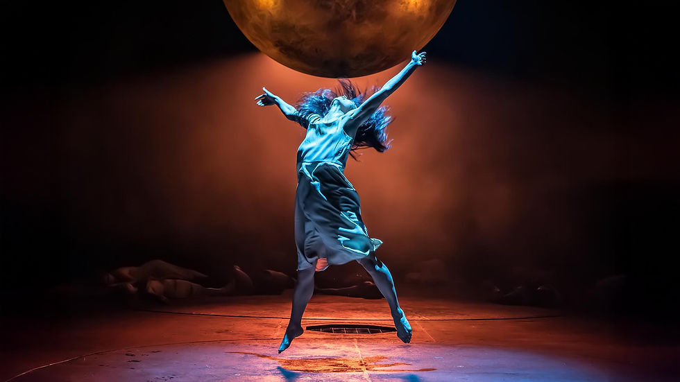 A dancer in a flowing dress leaps under a glowing orb in a dark, dramatic setting. Blue and orange lighting enhances the dynamic mood.