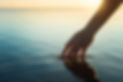 A female hand touching the ocean water in front of a beautful sunset during summer time..j