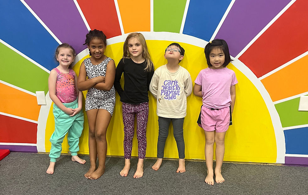Students in gymnastics class smiling by rainbow wall