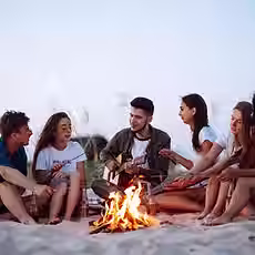 groupe-jeunes-amis-assis-plage-faire-frire-saucisses-homme-joue-guitare-temps-camping_2172