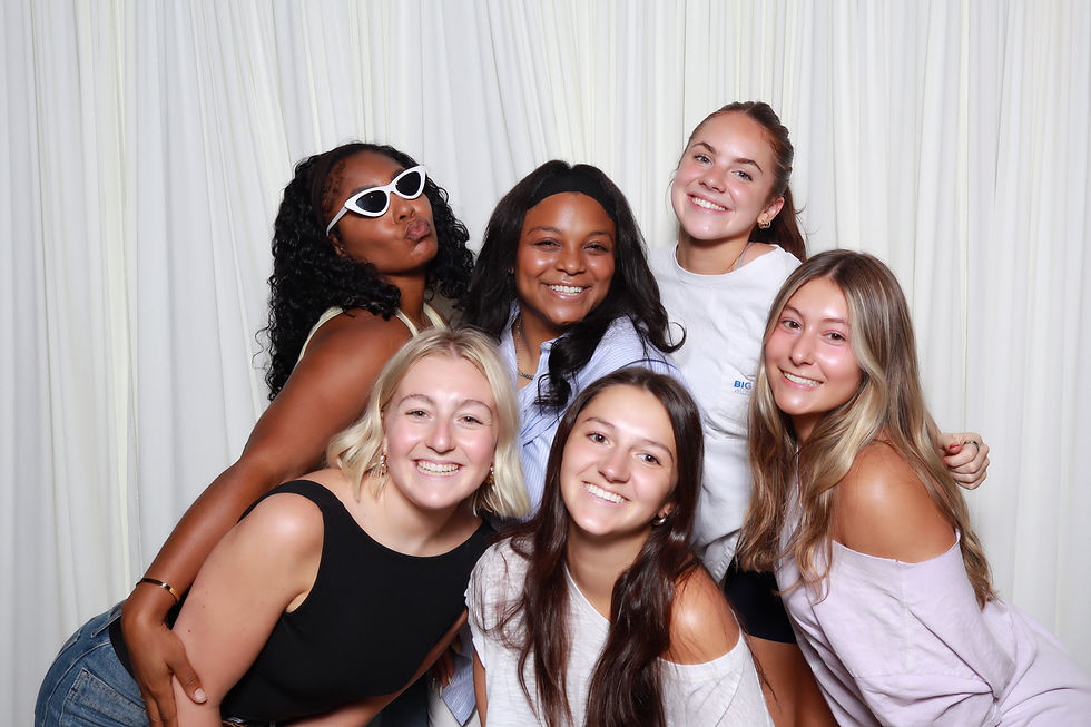 Six guests smiling and posing together in front of a white draped backdrop during a group photo booth experience.