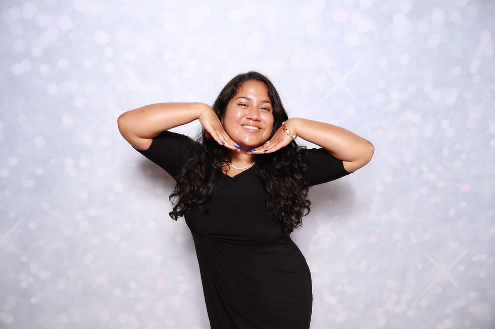 Jahely, A&A Booths lead photographer, smiling and posing in a black dress against a light studio backdrop.