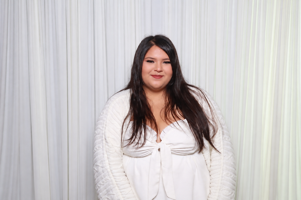 Alexa, A&A Booths photographer attendant, wearing a white outfit and smiling against a white studio backdrop.