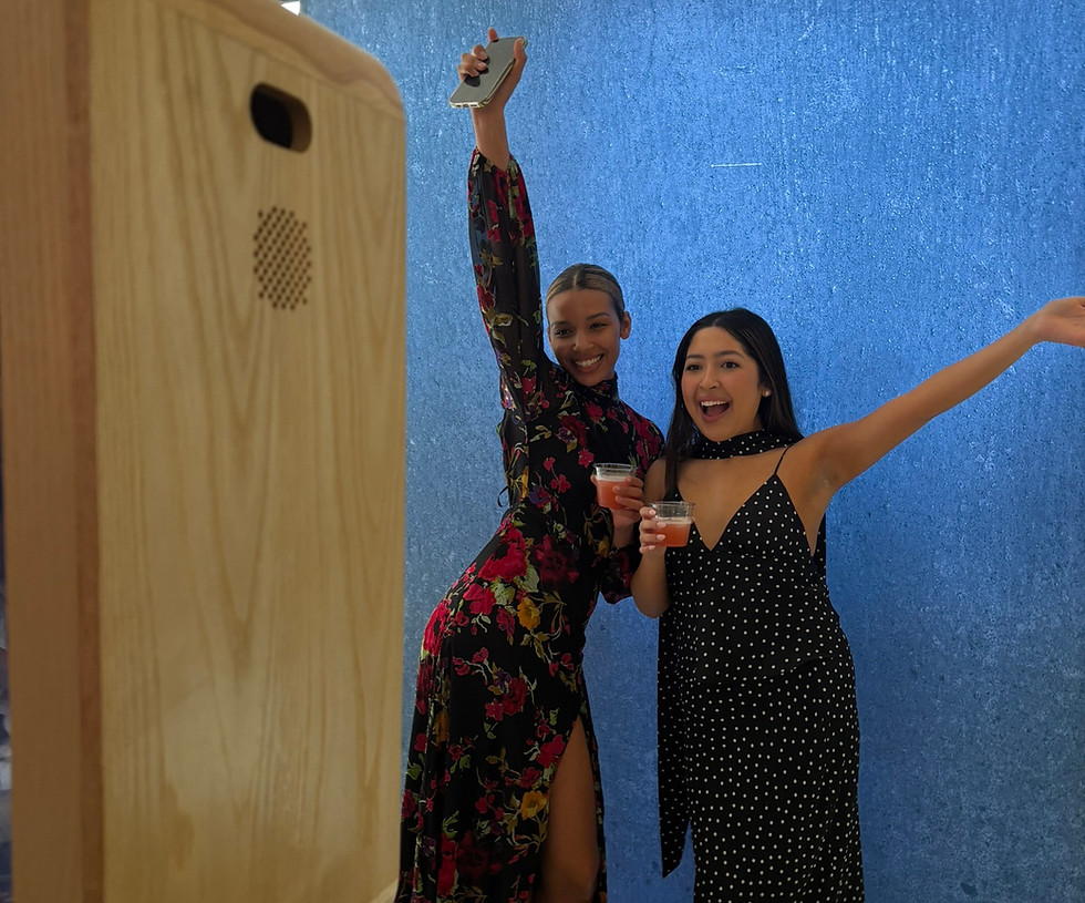 Two guests celebrating and posing in front of a wooden photo booth with a blue backdrop at an A&A Booths event.