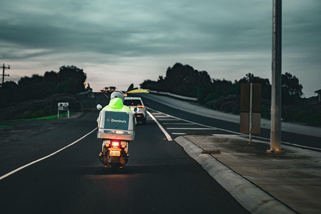 Domino's delivery scooter riding through a Melbourne street in Australia at dusk