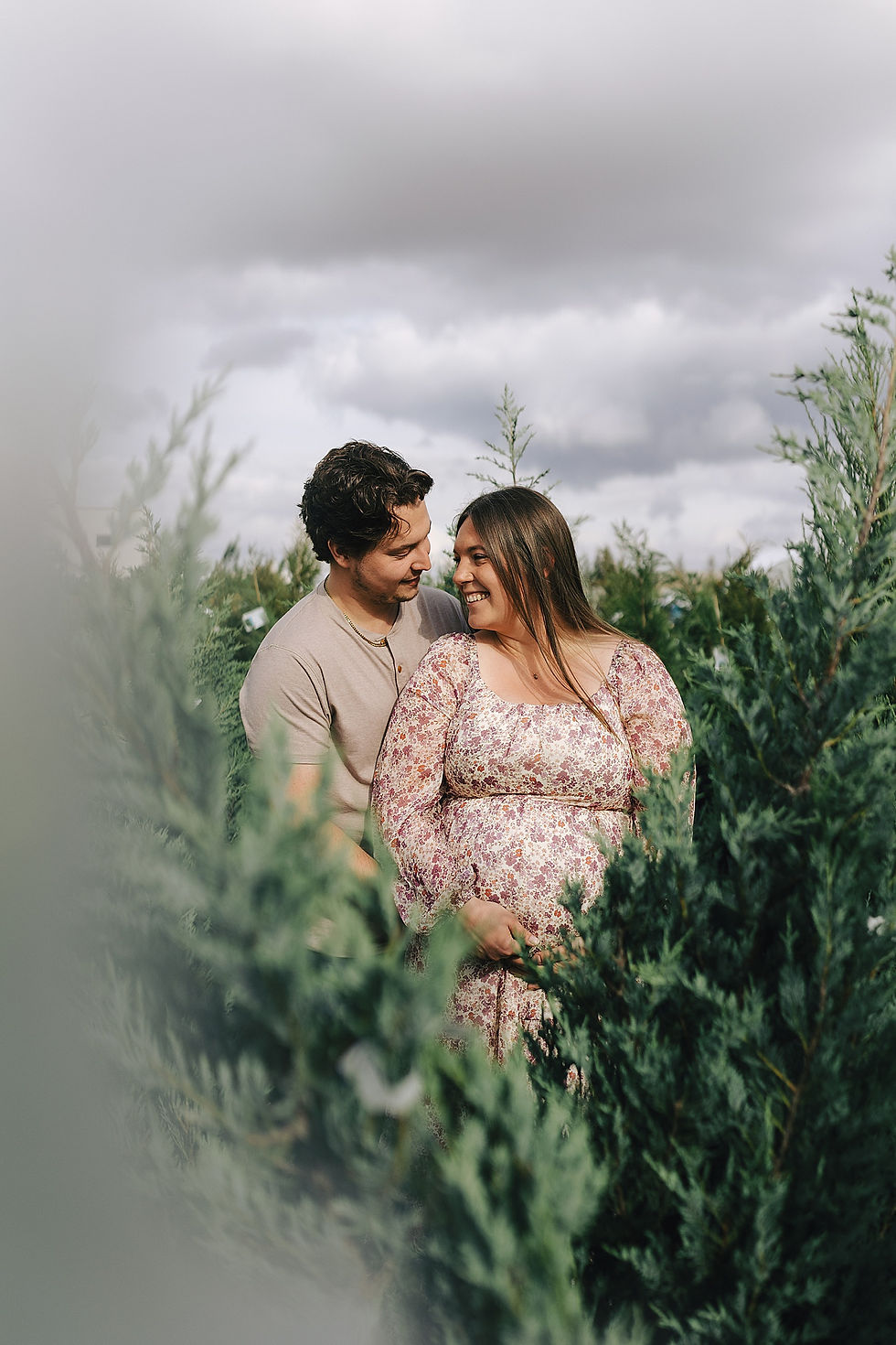 husband and wife cradle expecting belly surrounded by trees by Calgary portrait photographer