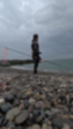 Spearfisherman standing on foggy, rocky beach with polespear