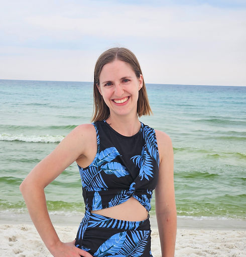 Woman in blue dress smiles at the camera on the beach with ocean.