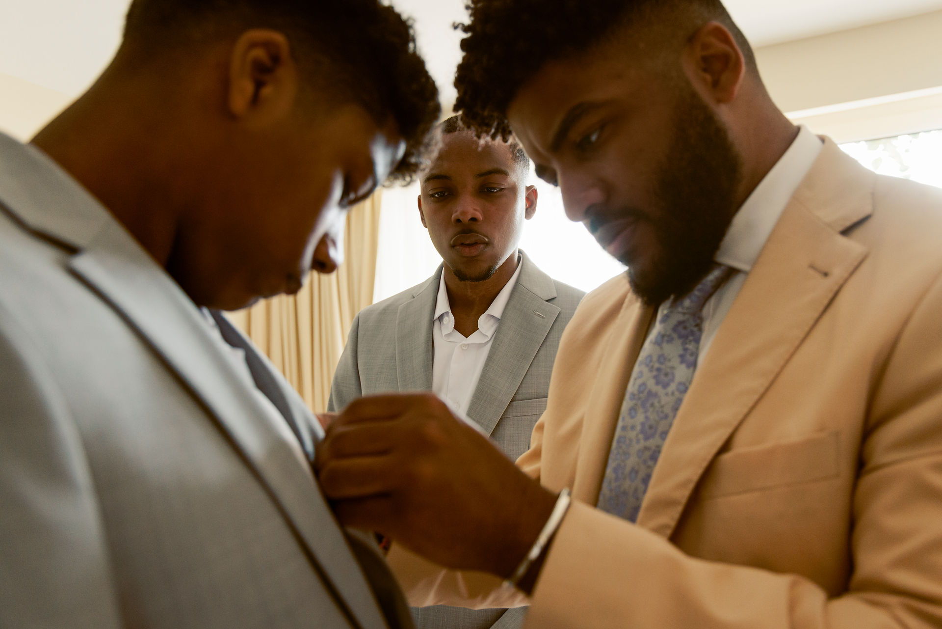 Groomsmen help adjust tie, wedding prep