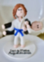 Clay figures of two people in judo outfits on a cake topper. One lifts the other. Karate Wedding Cake Topper 
