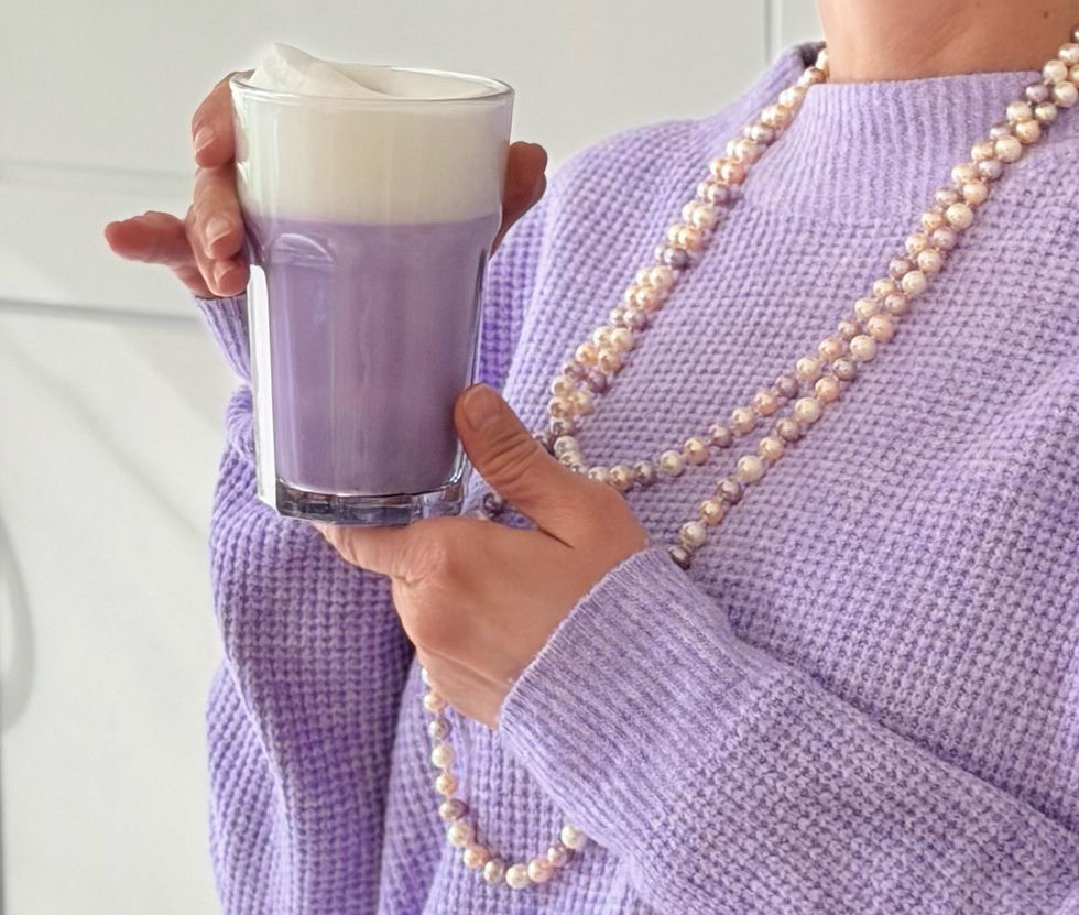 violetter Ube Latte  in der Hand von einer Dame mit violettem Pullover und Perlenkette