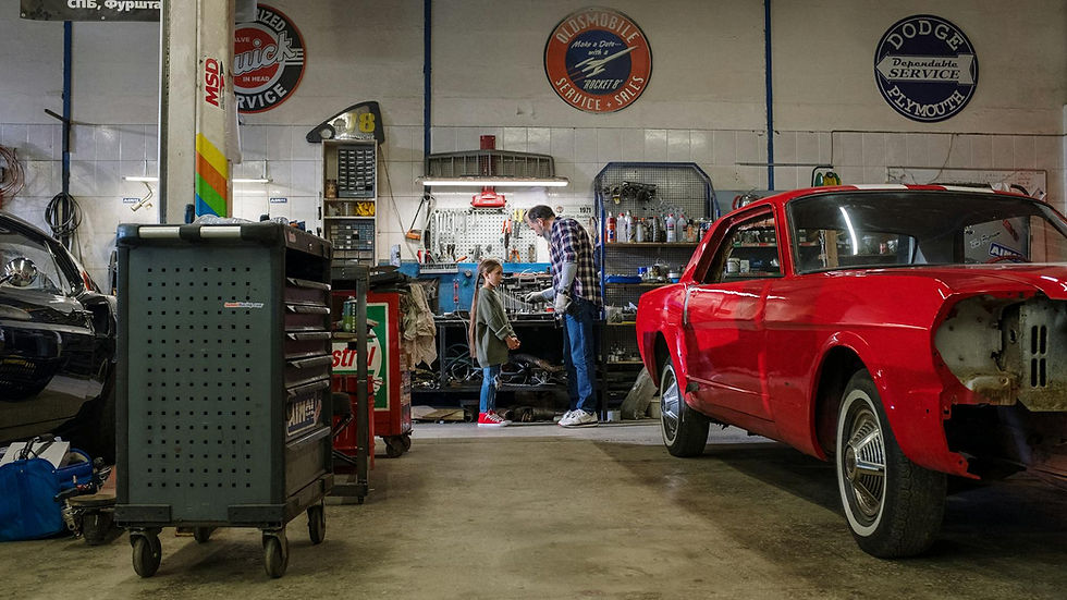 A father and daughter spend quality time together in a bustling auto repair shop, fixing cars.