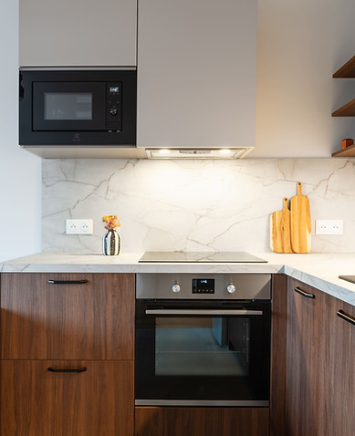 Zoom cuisine  meubles bas en noyer avec poignées noires et four - meuble haut beige clair sans poignée et  avec micro onde-  plan de travail et crédence effet marbre - hotte allumée au dessus de la plaque de cuisson