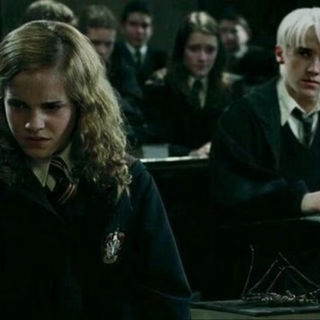 a personagem Hermione, em primeiro plano, com expressão de tristeza, com o personagem Draco Malfoy, ao fundo, olhando para ela