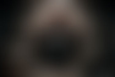 Homem de terno ajoelhado dentro de uma cela destruída, segurando correntes presas às mãos enquanto barras de ferro se rompem ao redor; um notebook aberto no chão sugere aprisionamento ligado ao trabalho.