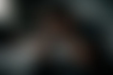 Homem sentado na beira da cama, segurando a cabeça com as mãos, em um quarto escuro e desorganizado, expressando exaustão física e emocional.