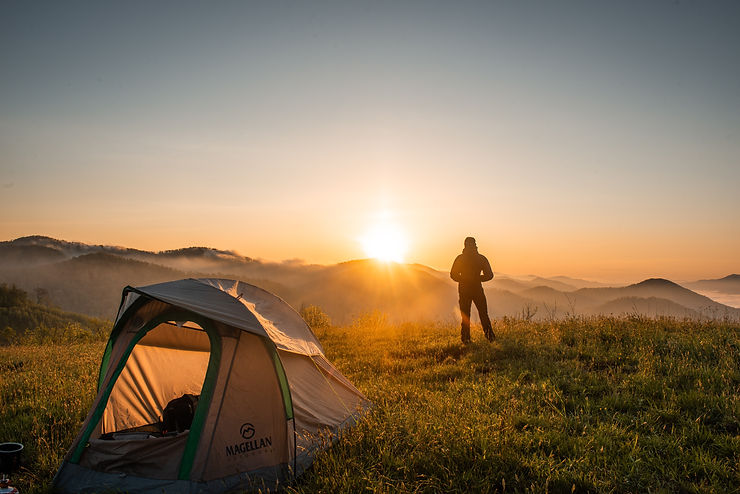 A man looking at a sunrise with a camp nearby