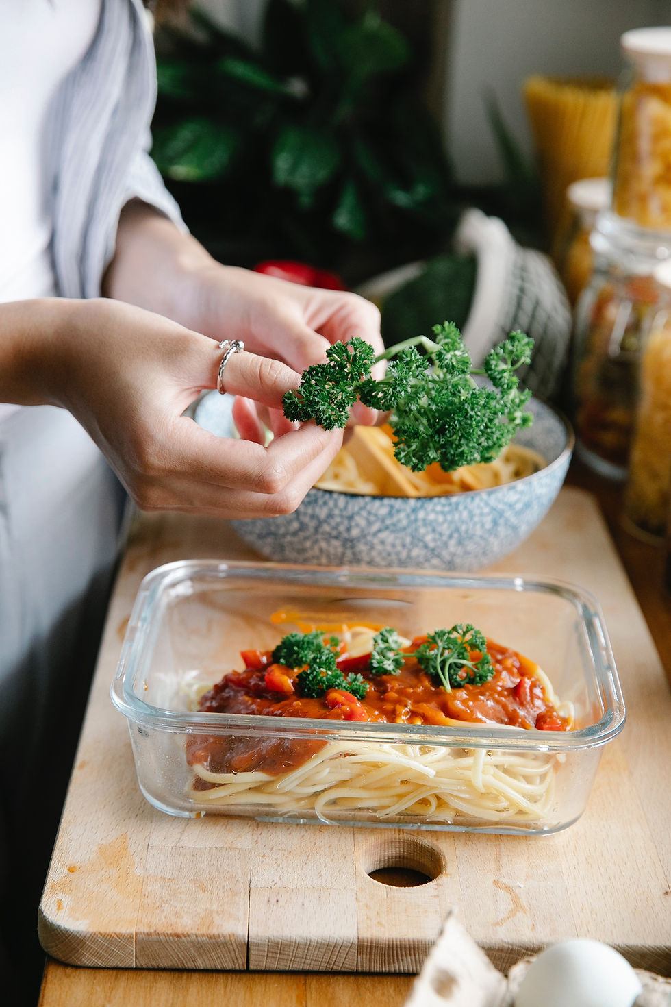 A woman putting vegetables in storage container filled with spaghetti