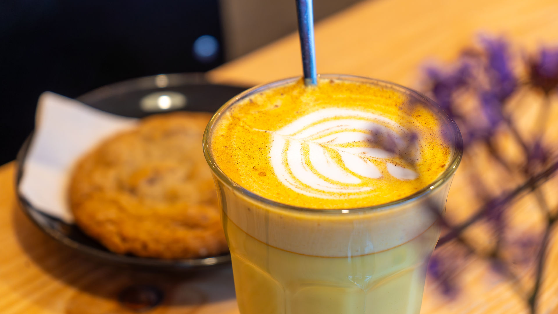 Golden turmeric latte in a glass with milk foam, paired with a lemon walnut cookie.