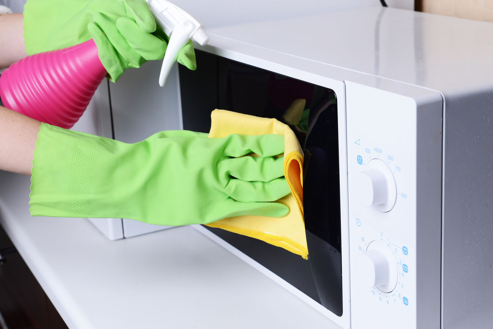 Person with green gloves cleaning a microwave with a spray bottle and cloth