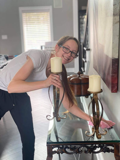 Woman smiling at the camera while dusting a glass table with a cloth