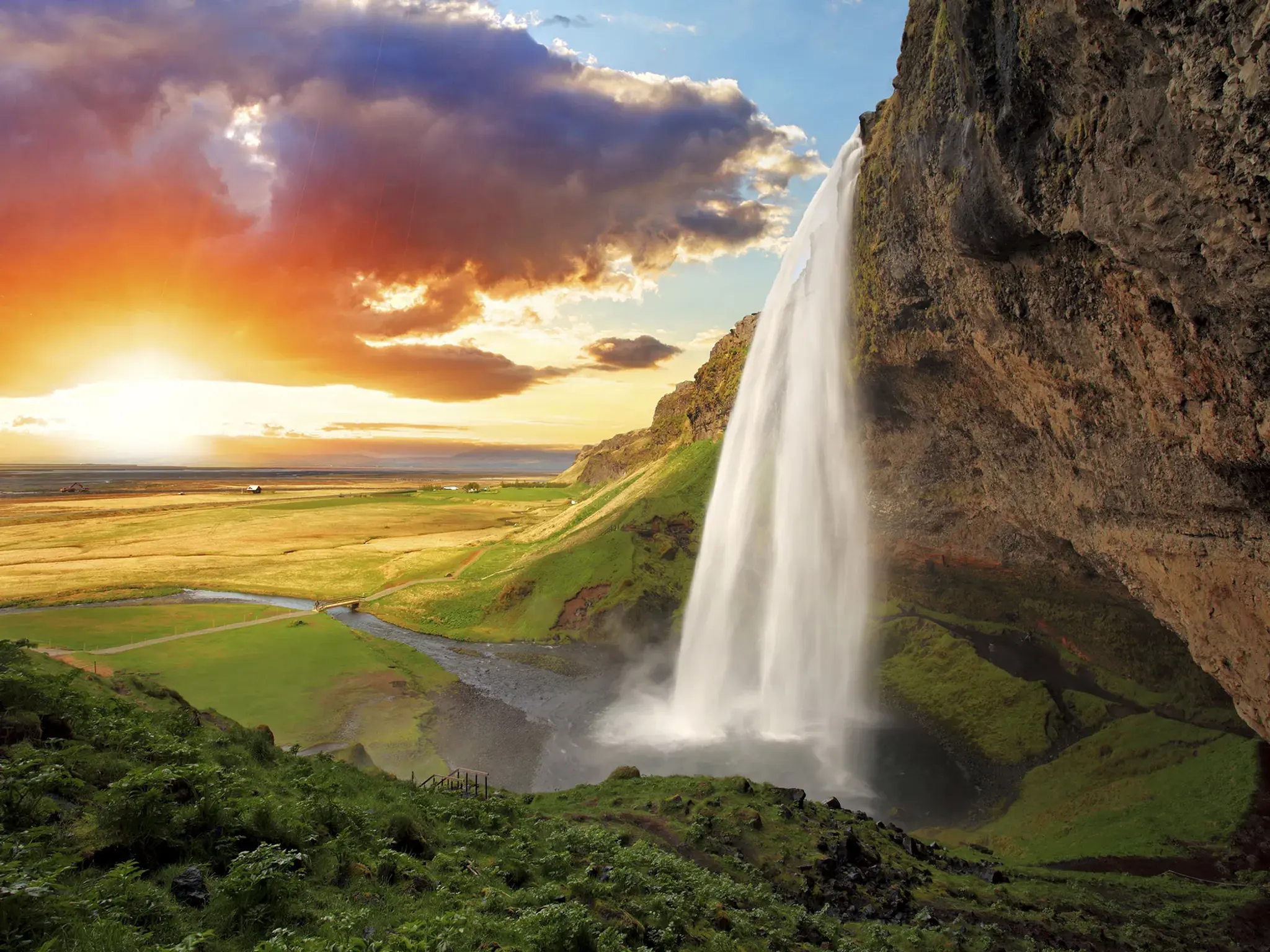Waterfall cascading down a cliff with a sunset in the background, scenic landscape