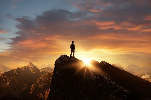 A Man standing on Mountain looking at Sun