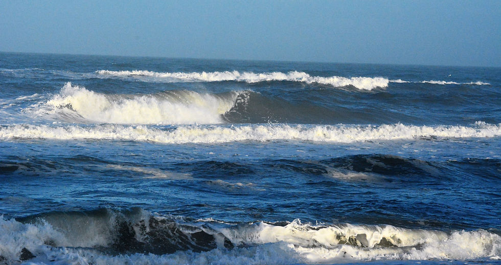 Rolling waves surge forward, showcasing the powerful force of the ocean tide against a clear blue sky.