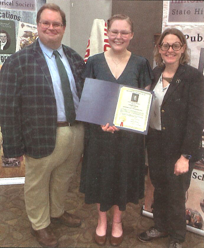 Scholarship recipient holding award with two presenters