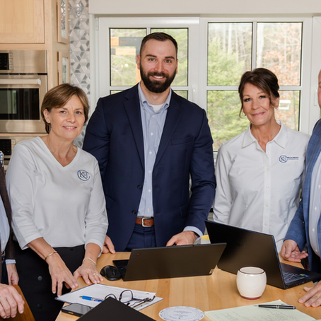The KRCrossing Consulting team gathered around a work table with laptops and documents, wearing branded KRC apparel, photographed at their Maine office