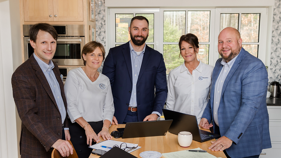 The KRCrossing Consulting team gathered around a work table with laptops and documents, wearing branded KRC apparel, photographed at their Maine office