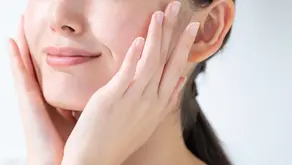 Close-up of a smiling woman with clear skin, gently touching her cheeks, used to illustrate rosacea and acne treatment options available in Singapore.