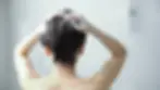 Woman shampooing her hair in a bathroom, focusing on scalp health for acne on scalp treatment.