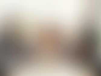 Group of nine real estate professionals in a bright office, engaged in a discussion around a table with papers. One person stands, gesturing confidently.