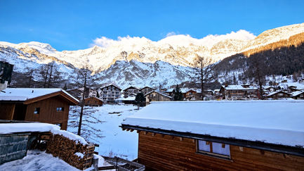 Blick vom Balkon auf verschneite Dächer und die Mischabelkette in Saas-Fee
