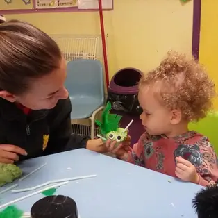 A young child with curly hair and a caregiver share a playful moment at a table