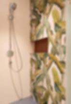 Shower with silver head and hose on a beige wall. Green leafy pattern on the adjacent wall.