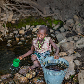 Young girl in Malawi collecting water in a bucket with a green cup