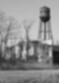 A building grown over with dead vines with a water tower in the background in black and white