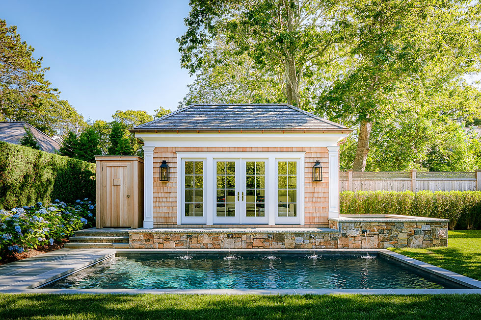Cedar shingle pool house with white French doors and a stone wall with water spouts above a pool on Martha's Vineyard